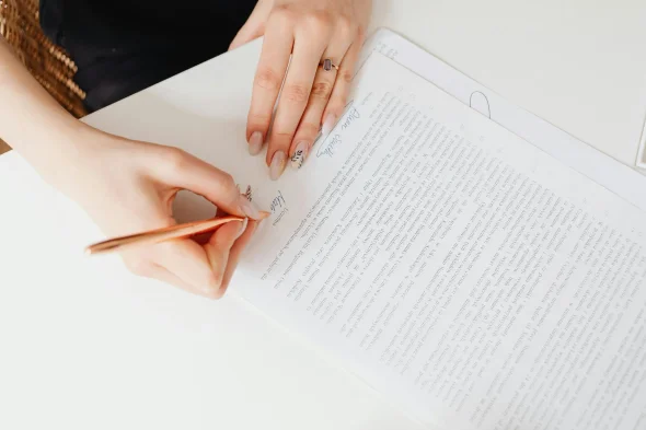 A person signing a document with a pen on a white desk.